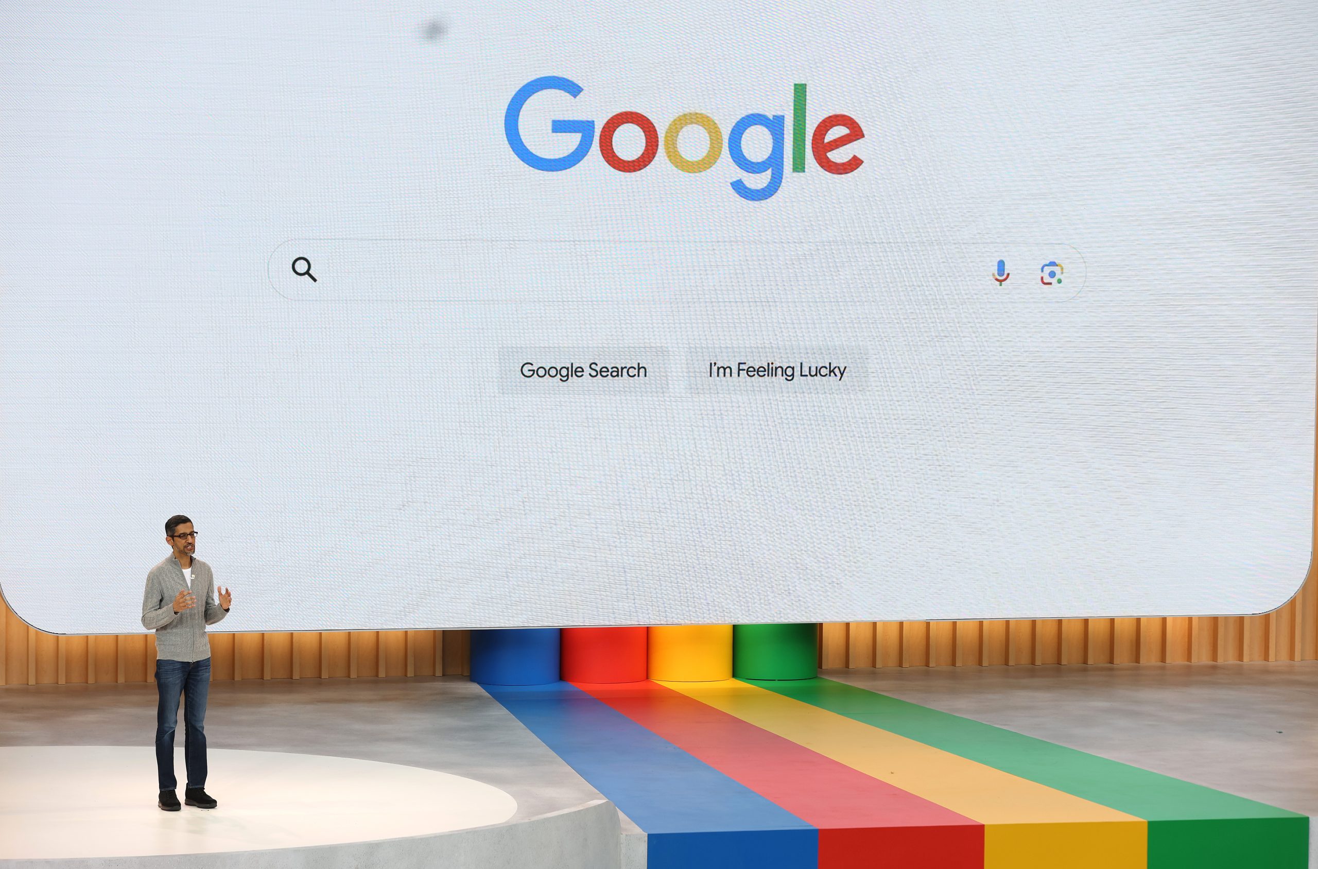 Redner vor großer Video-Wall mit Google-Logo und typischen Unternehmensfarben auf dem Boden