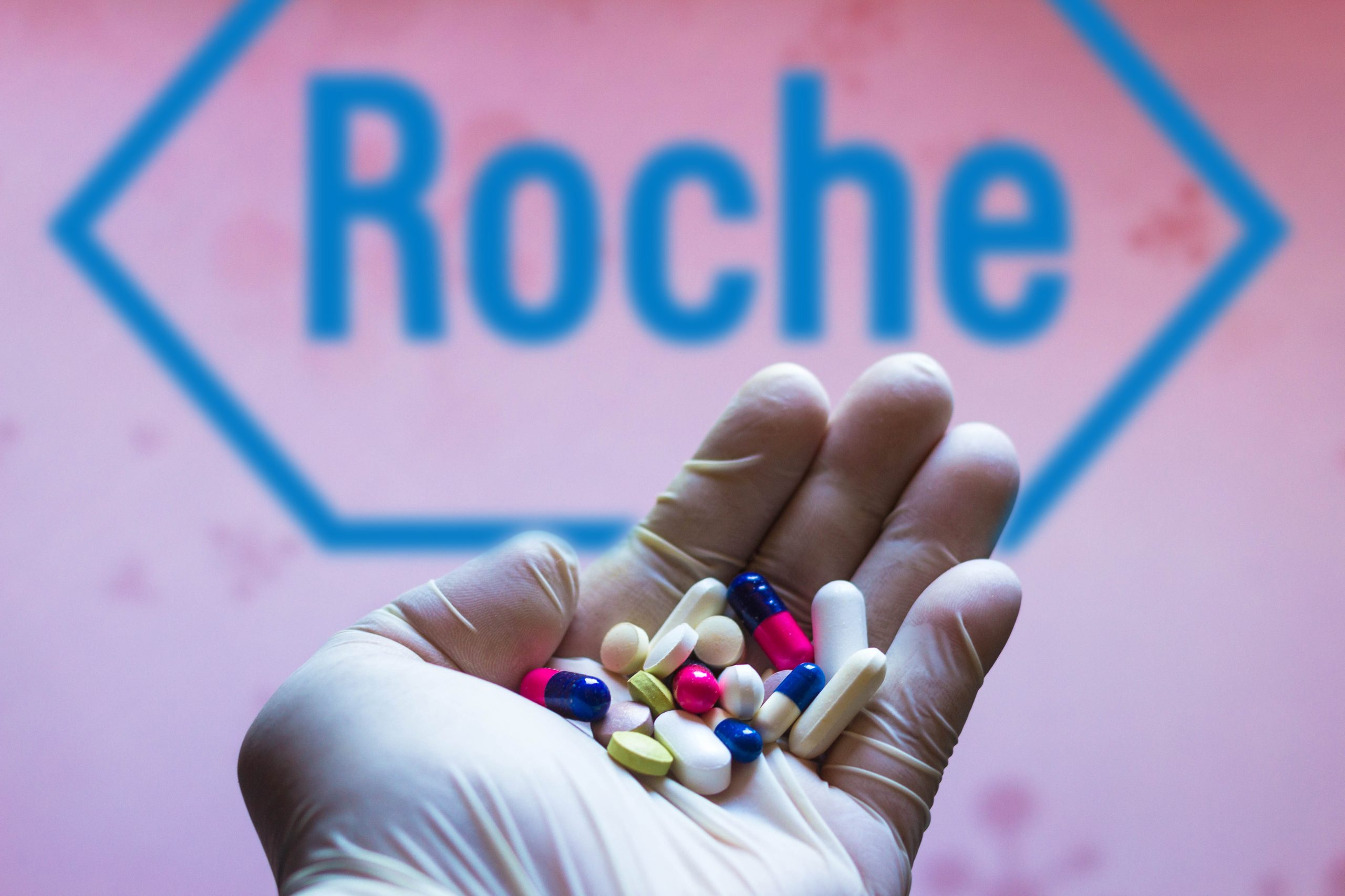 Hand mit Tabletten vor Roche-Firmenlogo