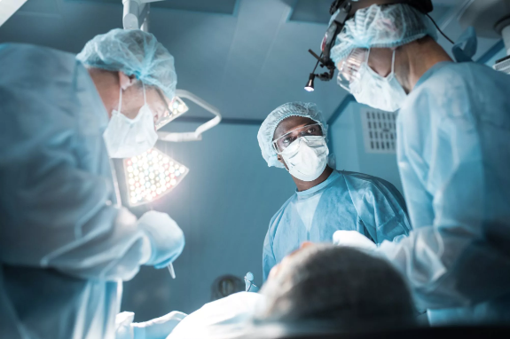 Drei Ärzte mit OP-Kleidung und Masken im Gesicht stehen im OP. Auf die OP-Tisch liegt eine Patientin