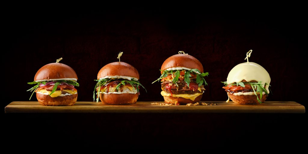 Drei Burger vor einem schwarzen Hintergrund und ein Burger mit Käse übergossen daneben.