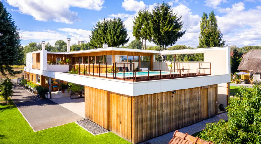 Modernes Familienhaus aus Holz mit Flachdach. Auf dem Dach ein Swimmingpool und eine Überdachung