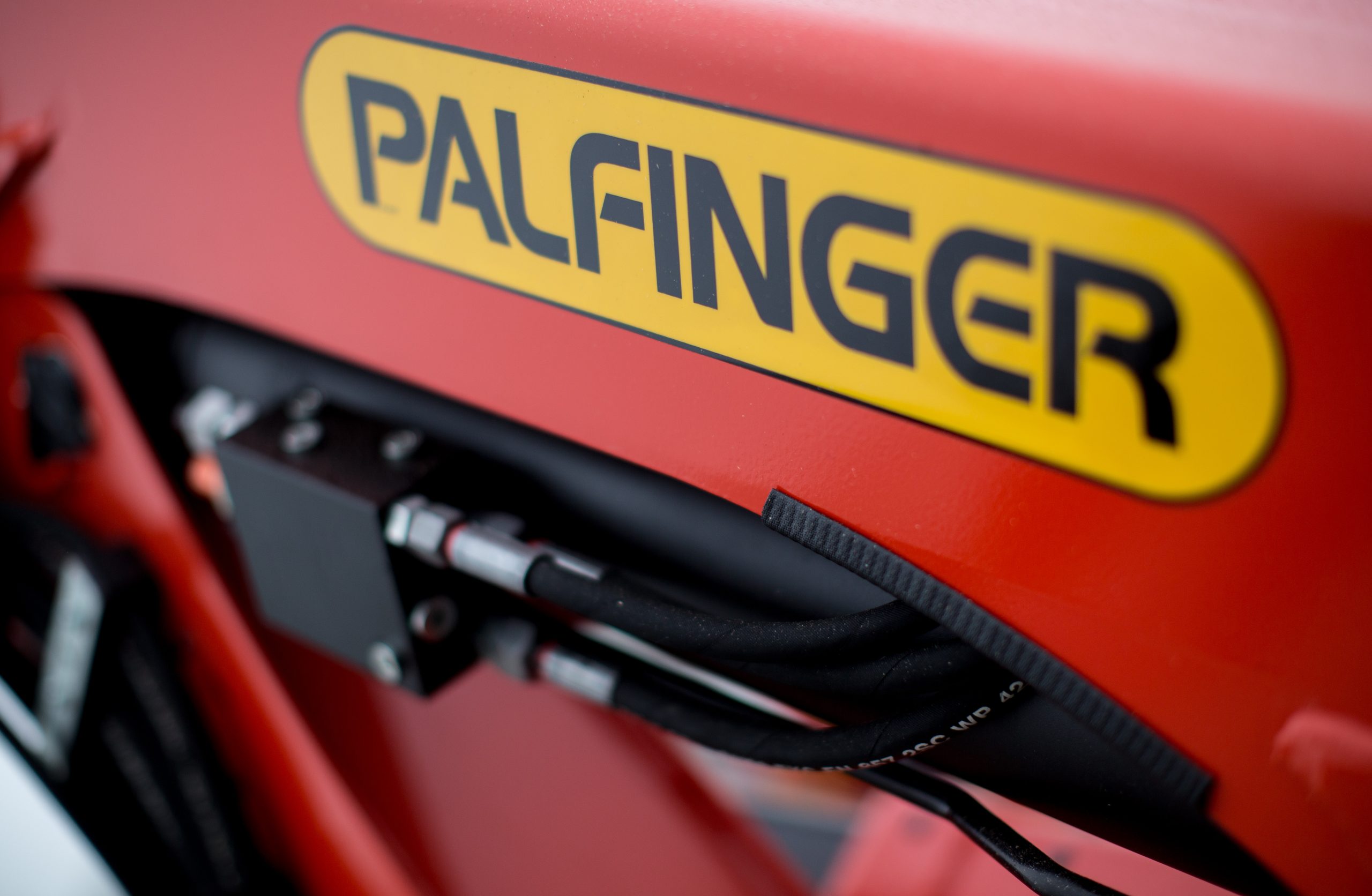 Logo von PALFINGER in schwarzen Buchstaben auf gelbem Hintergrund. Das Logo befindet sich auf einem roten Hintergrund