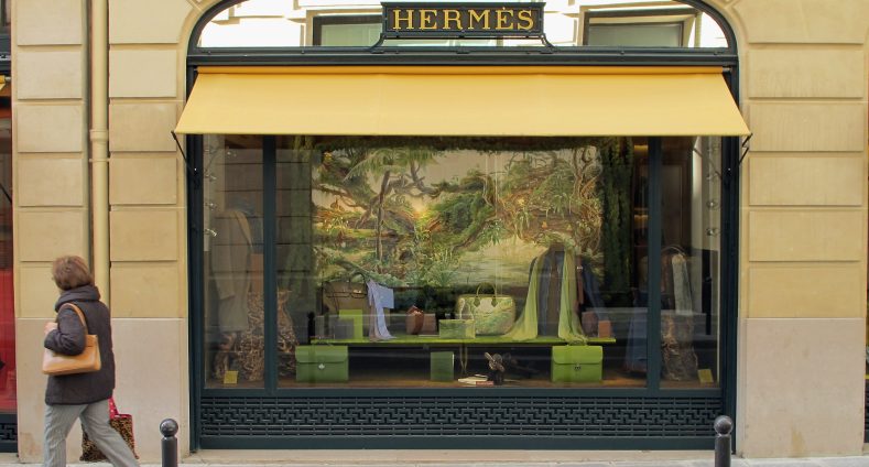 Eingang zu einer Hermès Filiale mit grünen Taschen und einem grünen Bild in der Auslage