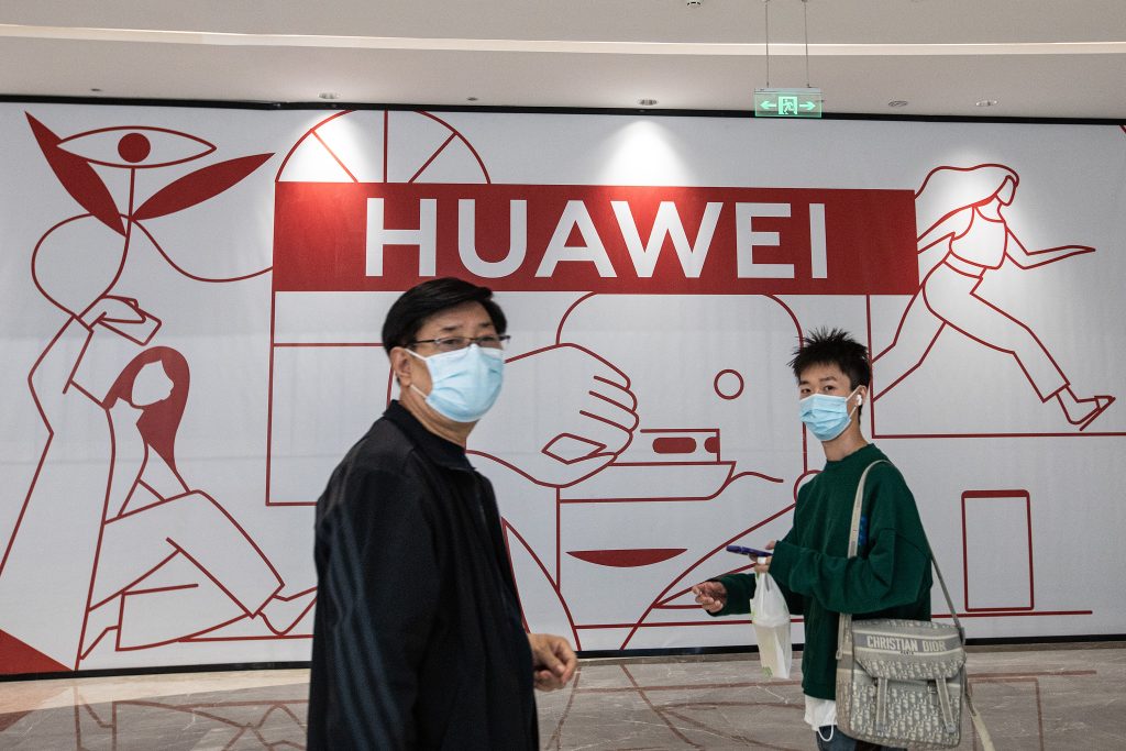 Logo von Huawei in rot. Davor zwei Männer mit Masken aus China