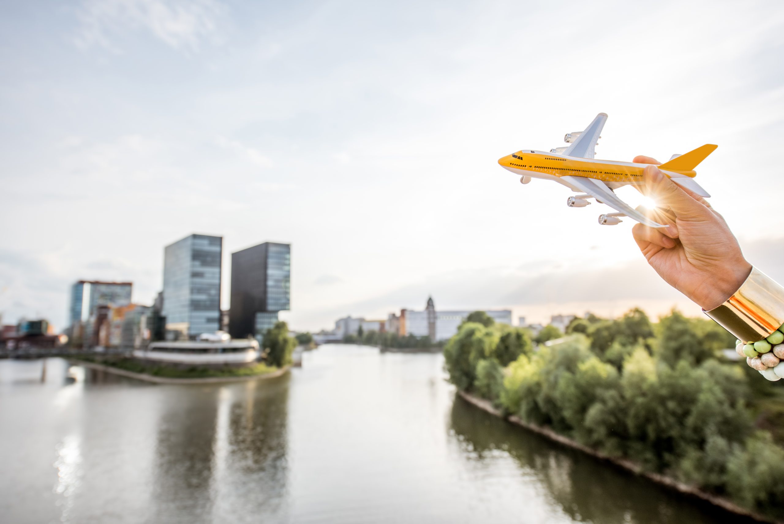 Häuserfront und ein See davor. Im Vordergrund eine Hand die ein Mobilflugzeug hält