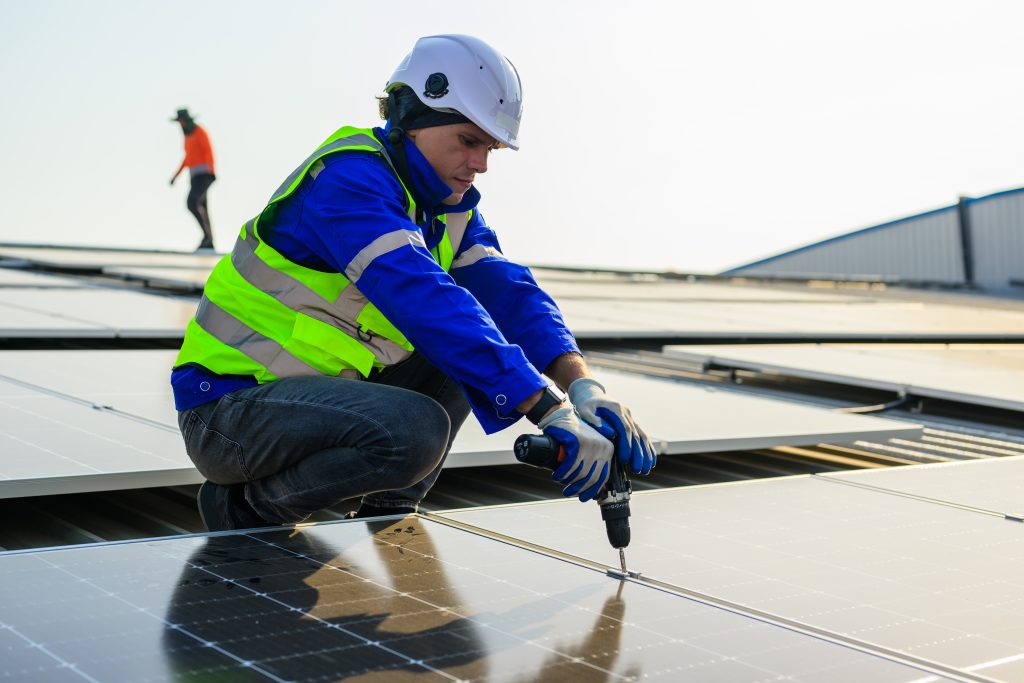 Man mit weißem Schutzhelm und blauer Jacke montiert eine Solarpanele