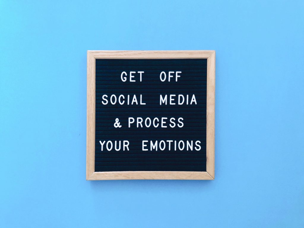 blauer Hintergrund und ein Schild mit der Aufschrift: Get off social Media & Process your emotions