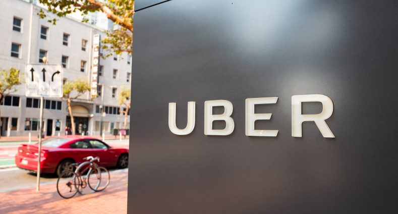 Logo von Uber und dahinter ein Auto in rot und Gebäude