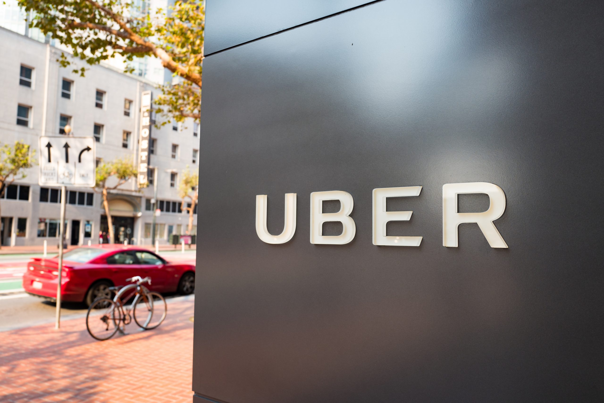 Logo von Uber und dahinter ein Auto in rot und Gebäude